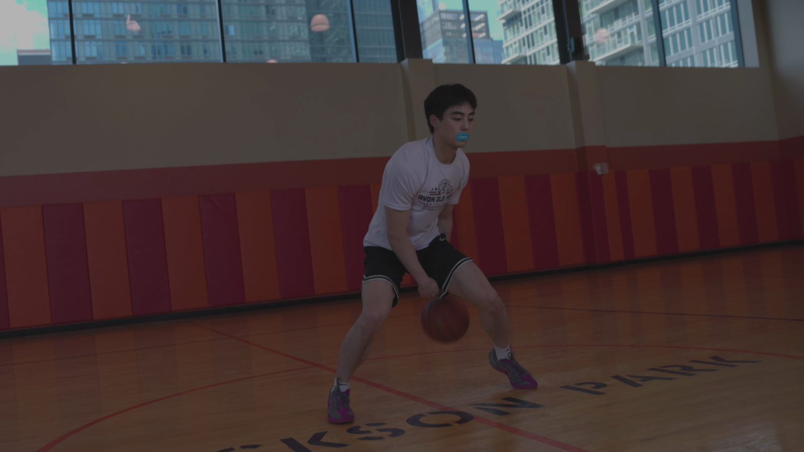 Person playing basketball in an indoor court with colorful walls and a cityscape view.